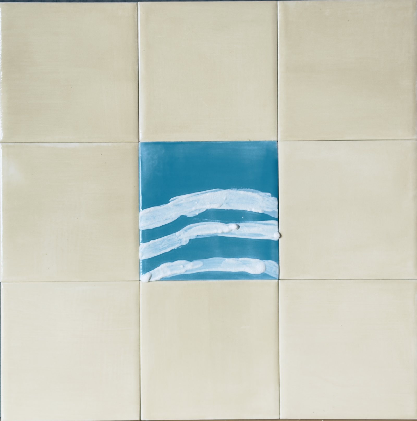 Nine cream tiles with a single aquamarine centre tile carrying three white waves.