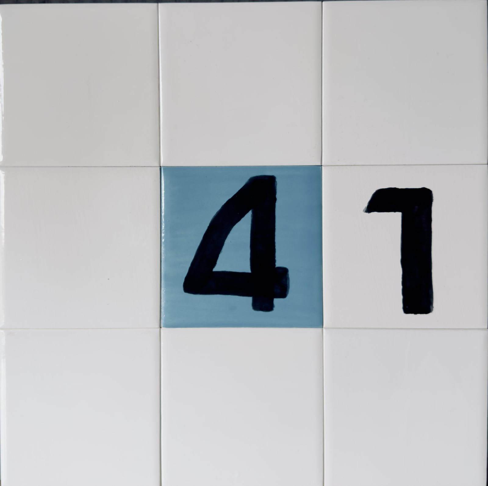 A nine by nine grid of off-white tiles with hand-painted black numerals and six blue glazed tiles.