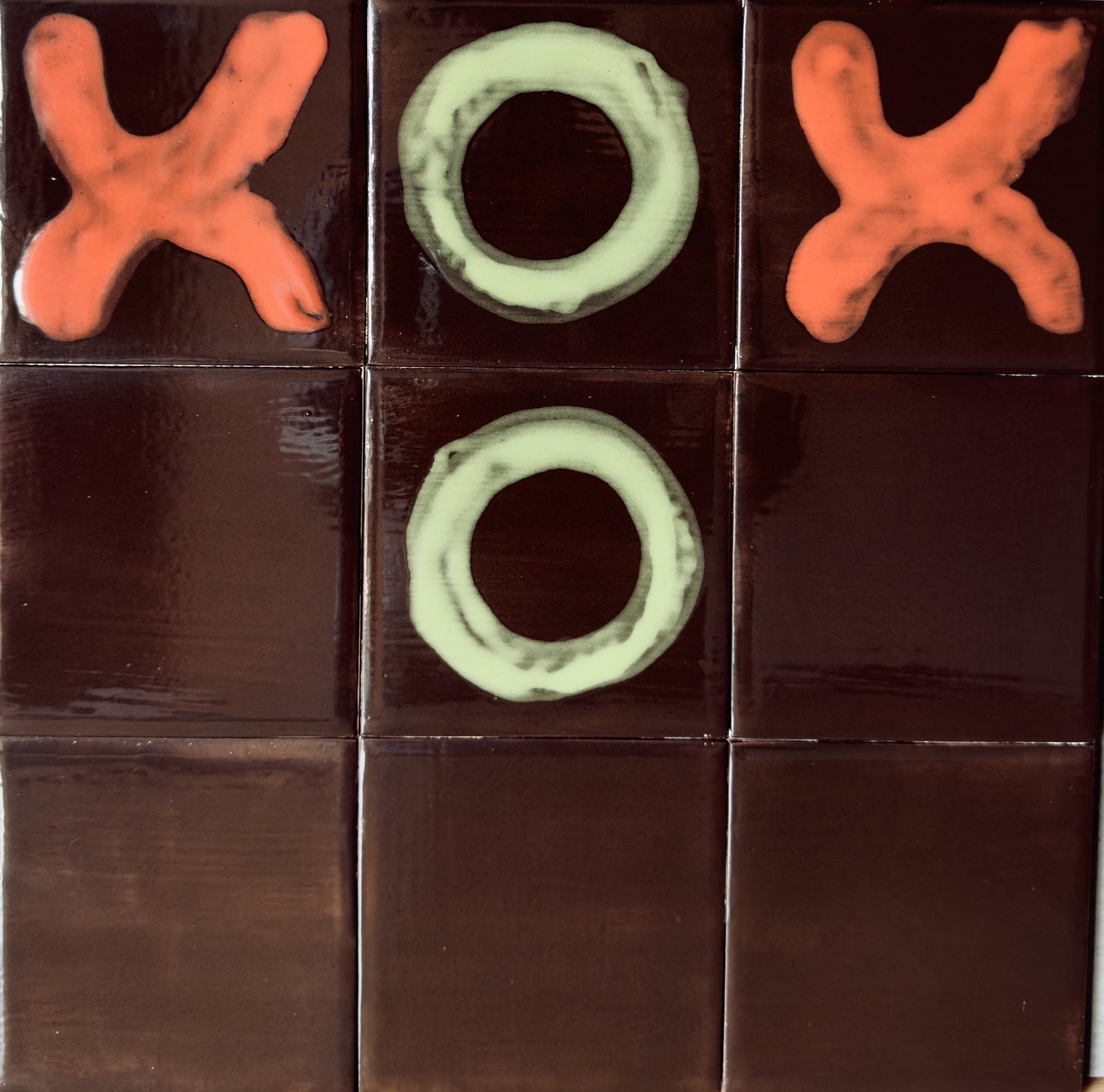 Nine dark oxblood tiles hand-painted with coral crosses and lime noughts.